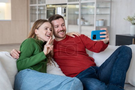 Photo for Positive merry glad couple looking at phone camera, having video call with friends, doing selfie shot on smartphone, making profile picture for social networks, taking photo for sending to relatives - Royalty Free Image