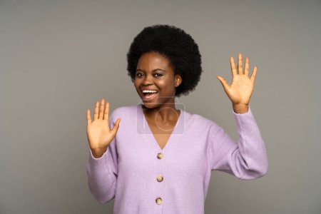 Téléchargez les photos : Optimiste gai afro-américaine femme ont humour amusant montrant paumes, souriant largement. Femme noire ravie avec coiffure bouclée heurtant un mur invisible comme un mime sur fond de studio gris. - en image libre de droit