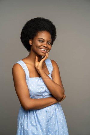 Photo for Charismatic merry dark skinned african female with natural curly hair, unusual white teeth, smiling with cheek dimples. Optimistic female wearing summer dress, isolated on grey studio background - Royalty Free Image