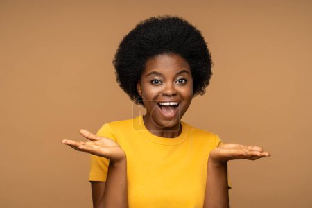 Photo for Happy glad cheerful smiling dark skinned woman with curly hairstyle, unusual white teeth, expression of joy and happiness on face, looking at camera, posing for picture, holding palms opened isolated. - Royalty Free Image