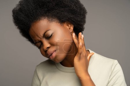 Téléchargez les photos : Femme afro-américaine touchant ganglions lymphatiques hypertrophiés sous l'oreille sur le cou. Douleur, douleur, gêne près de la mâchoire, ayant des symptômes d'amygdales enflammées, virus du sar, rhume, sialadénite - en image libre de droit