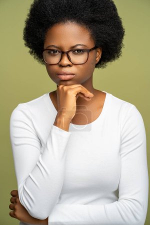 Téléchargez les photos : Femme afro-américaine confiante sérieuse dans des lunettes avec un regard strict tendu ressemblant à leader, femme d'affaires, gestionnaire, enseignant. Femme noire perplexe réfléchie isolée sur fond de studio vert - en image libre de droit