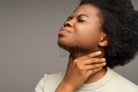 Téléchargez les photos : Femme afro-américaine souffrant de maux de gorge, d'inconfort à avaler, de perte de voix. Malade féminin touchant le cou avec expression douloureuse du visage causée par une infection respiratoire, laryngite, amygdalite - en image libre de droit