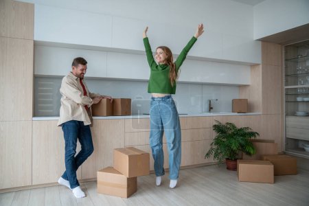 Joyous married couple embarks on new chapter as move into new home. Pleased husband and overjoyed wife share triumphant look moving to new light apartment. Happy woman joy jumping feeling housewarming