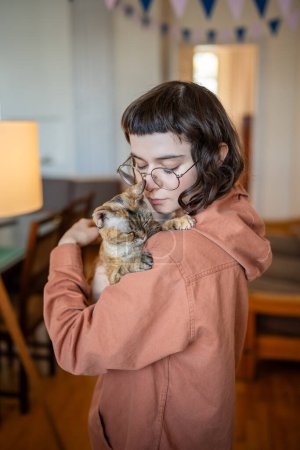 Caring pet owner tenderly hugs cute Devon Rex cat supporting each other. Kind young woman affectionately holds stray cat has found new home. Warm friendly embrace between domestic animal and teen girl