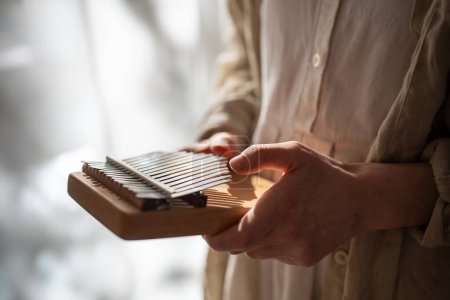 Closeup hands playing on kalimba in sunlight. Ethnic musical instrument for producing sound relaxation melody on metal keys. African finger piano in modern life. Stress relieve with instrumental music