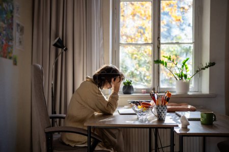Photo for Exhausted depressed woman with professional burnout sitting at table holding head with hands trying start work. Tired unwell young female feeling bad having dizziness headache sitting at desk at home - Royalty Free Image