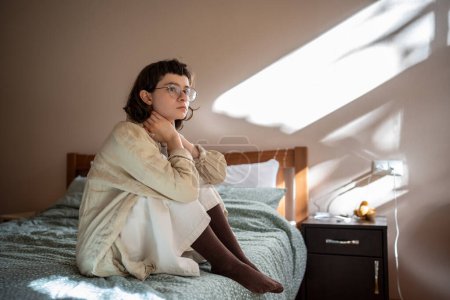 Photo for Melancholic lonely teen girl sits on bed, sadly looking at window, feeling anxiety depression. Frustrated worried teenager thinking about school bullying. Adolescence, puberty, awkward age troubles. - Royalty Free Image