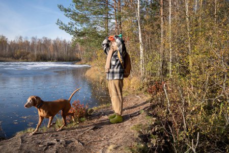 Satisfied happy female hunting dog owner enjoy walk domestic animal by forest lake on sunny warm day. Pleased woman watching playful, active Magyar magyar vizsla pet running along shore of forest pond