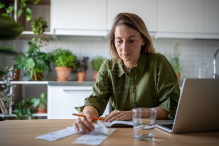 Accountant working freelance at home sitting at table, doing company annual financial statement. Thoughtful female checking bills, receipts, doing paperwork for insurances, taxes, credits payment.