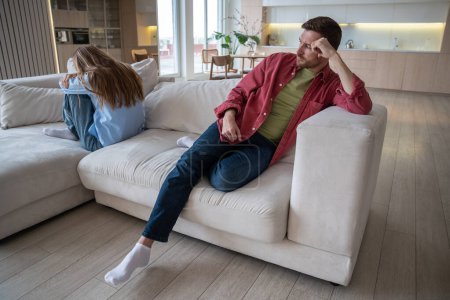 Boyfriend and girlfriend having quarrel sits on sofa in offended positions. Body language shows anger and frustration due conflict. Man and woman immersed in thoughts not daring to speak feel offended