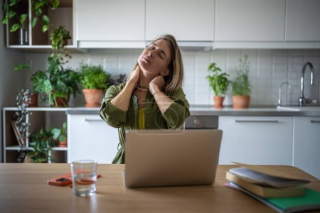 Tired overworked woman sits at table with laptop massaging neck, relaxing after hard job. Exhausted female freelancer having spine discomfort, muscle tension caused by uncomfortable sitting position.