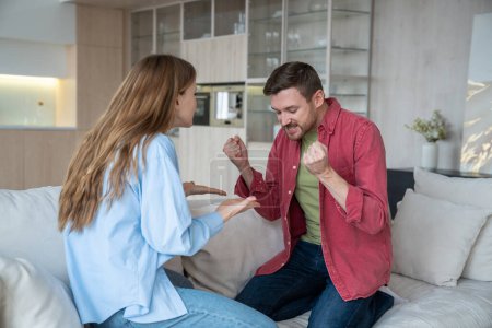 Violent emotional quarrel occurs home between man woman sitting on sofa opposite each other. Gesturing couple heatedly express mutual claims their faces express irritation. Serious cause of conflict.