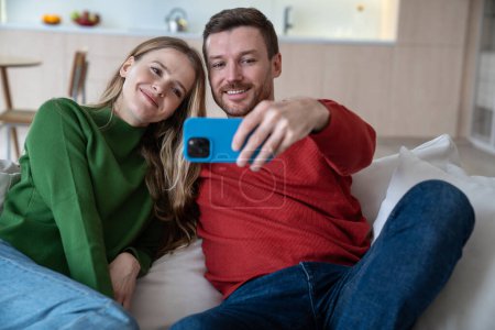 Photo for Guy and girlfriend sit comfortably on soft sofa take joint selfies mobile phone capturing joyful moments. Lovers decided to share atmosphere happiness strong relationship with friends and loved ones. - Royalty Free Image