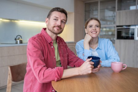 Photo for Loving couple sitting in cozy kitchen with cups aromatic coffee, immersed dreams happy future. Boyfriend girlfriend making plans for life together full joyful events. Couple faces glow with happiness. - Royalty Free Image