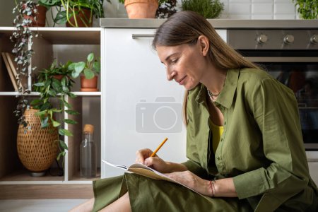 Téléchargez les photos : Femme concentrée réfléchit sur les pensées, les écrivant dans un carnet après la séance de thérapie. Femme engagée écrit des notes pour la compréhension de soi dans un environnement détendu. Se connaître pour la vie de bien-être - en image libre de droit