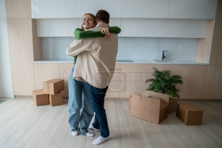 Photo for Cheerful inspired husband and wife happy embrace among unpacked things, celebrating long-awaited move to new home. Couple sincere hugs with love and hope for wonderful future in cozy family apartment. - Royalty Free Image