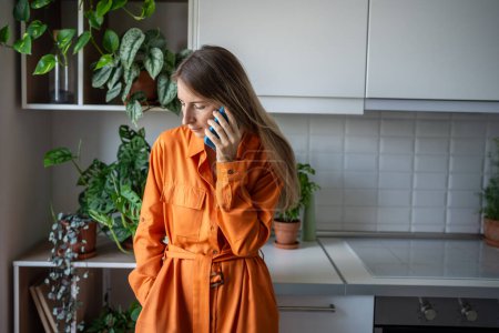 Distraught woman trying to make important phone call run around in head with worried thoughts. Upset female have unpleasant conversation on mobile phone standing on kitchen at home with indoor plants.