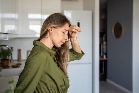 Photo for Unwell tired middle aged woman feeling head hurt rubbing forehead standing with closed eyes at home. Unhealthy exhausted female suffering from migraine, head pain, headache, cephalalgia, dizziness. - Royalty Free Image