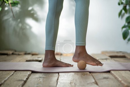 Photo for Legs rolling fitness ball on yoga mat. African American woman self care work out with myofascial massage ball, rolling feet, relaxing and improving circulation. Sports equipment for healthy lifestyle. - Royalty Free Image