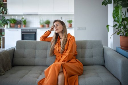Photo for Relaxed thoughtful woman sitting on couch looking aside daydreaming at home. Pleased middle aged female enjoy lazy weekend in calm. Pensive housewife resting feels satisfied after chores housework. - Royalty Free Image