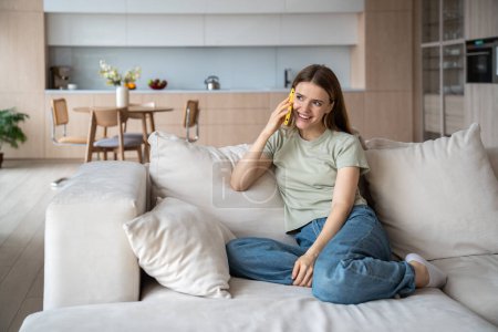 Photo for Carefree cheerful merry middle-aged woman sitting on comfortable sofa at home, talking on mobile phone, telling, listening to gossips, having pleasant conversation, discussion with friend. Slow life. - Royalty Free Image