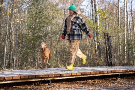 Happy woman dog running, walking enjoying nature on ecological trail in nature park on wooden path. Positive pet owner female traveling with dog friend together. 