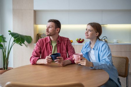 Loving couple sitting in cozy kitchen with cups aromatic coffee, immersed dreams happy future, looking at window. Boyfriend girlfriend making plans for life together full joyful events. 