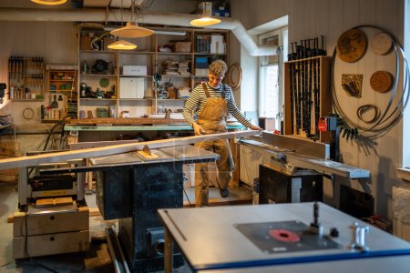 Téléchargez les photos : Carpentry workshop, craftsman master working with circular saw. Guy on workplace with large processed piece of wood. Joinery, man uses professional level skills talents to create functional woodwork. - en image libre de droit