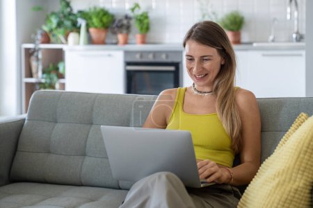 Photo for Happy woman sitting with laptop on lap on sofa receive interesting good news. Satisfied cheerful female with portable computer on knees chatting in social media, online shopping, have fun in internet. - Royalty Free Image