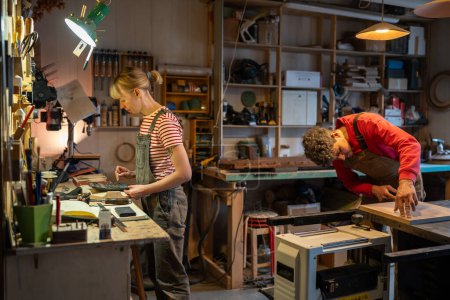 Family carpentry workshop, young couple of carpenters working on wood in studio with wooden items, equipment and tools. Business owner, entrepreneur, woodworking industry concept