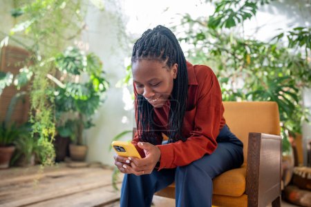 Satisfied contented african american woman smiling looking on screen smartphone enjoy online communication in urban jungle interior. Happy black young female chatting in social network on cellphone.