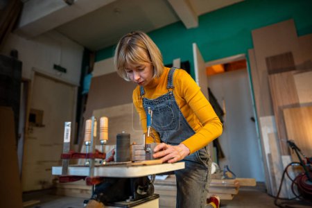 Femme charpentier concentré tourne des produits en bois faits main. Intéressé menuisier féminin concentré précautions de sécurité réfléchies fait partie des meubles d'artisanat sur tour. Travail du bois dans les petites entreprises