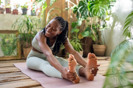 Photo for Joyful african american woman stretching, practice yoga. Happy black girl doing pilates workout for good figure. Cheerful female enjoy fitness in urban jungle home garden for flexibility body strength - Royalty Free Image