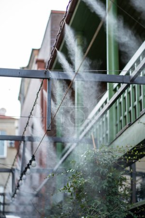 Nebelmaschine auf öffentlichem Platz installiert, um überhitzte Luft abzukühlen. Sprüher Wassernebel Ausrüstung im Freien. Klimaanlage, Wassersprühsystem für die Terrasse. Vernebeln, befeuchten, kühlende Luft.