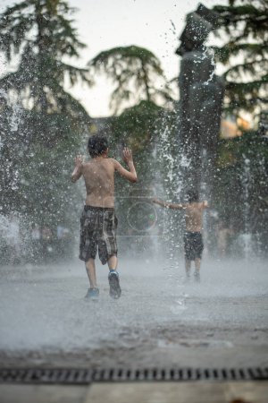 Children playing happily in city fountain, seeking relief from scorching summer heat. Joyful kids delight in refresh water, finding respite from sultry, enjoy carefree escape from hot sweltering day.