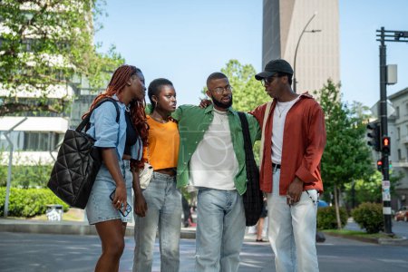Le gars afro-américain détendu partage avec enthousiasme une histoire intéressante de commérage avec des amis alors qu'il marche après avoir étudié. Groupe satisfait d'étudiants noirs, se reposant et bavardant, profiter du temps de promenade ensemble.