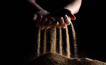 Hand releasing dropping sand. Fine Sand flowing pouring through fingers against black background. Summer beach holiday vacation and time passing concept. Isolated high speed shutter