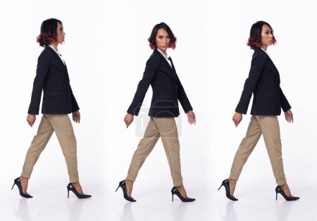 Foto de Medio cuerpo 20s mujer asiática usar formal vestido de negocios blazer zapatos de tacón alto. Negro pelo rizado corto femenino caminar sonrisa feliz, caminando hacia adelante a la izquierda derecha sobre fondo blanco aislado - Imagen libre de derechos