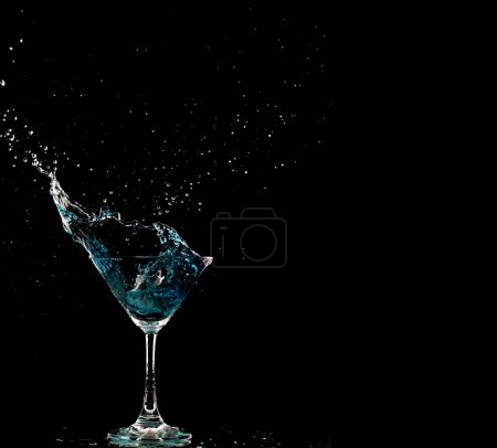 Foto de Azul vaso de cóctel con salpicaduras de alcohol de agua, cristal cóctel bebida salpicadura salpicadura en el aire y burbuja de vidrio. Licor Parte congelación disparo de alta velocidad sobre fondo negro aislado - Imagen libre de derechos
