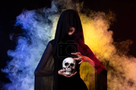 Photo for Old Witch costume woman craft spell horror magic on Horror night with Evil makeup face Art scary Magician smoke skull death hands. Colorful fog smoke over black background copy space - Royalty Free Image