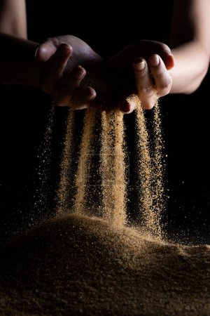 Photo for Hand releasing dropping sand. Fine Sand flowing pouring through fingers against black background. Summer beach holiday vacation and time passing concept. Isolated high speed shutter - Royalty Free Image