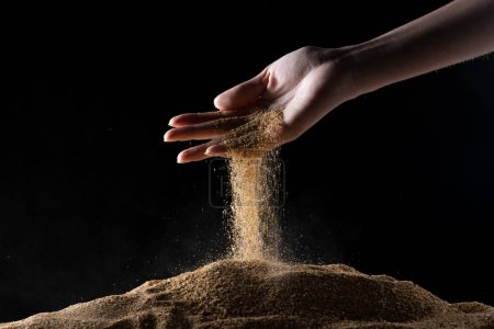 Photo for Hand releasing dropping sand. Fine Sand flowing pouring through fingers against black background. Summer beach holiday vacation and time passing concept. Isolated high speed shutter - Royalty Free Image