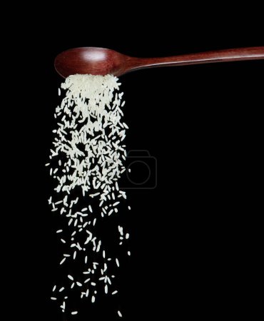 Foto de Caída de arroz japonés, los arroces de grano blanco vertiendo nubes abstractas vuelan desde la cuchara. Hermoso arroz de semilla completa en el aire, diseño de objetos alimenticios. Congelación de enfoque selectivo tiro Fondo negro aislado - Imagen libre de derechos
