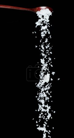 Foto de Caída de sal, cacahuetes de grano blanco cristal explotan nube abstracta volar de cuchara de madera. Hermosa sal de semilla completa, diseño de objetos alimenticios. Congelación de enfoque selectivo tiro fondo negro aislado - Imagen libre de derechos