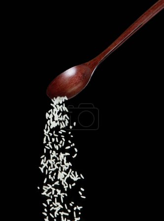 Téléchargez les photos : Japanese Rice fall, white grain rices versing down abstract cloud fly from spoon. Belle graine complète de riz dans l'air, design objet alimentaire. Mise au point sélective prise de vue au gel Fond noir isolé - en image libre de droit