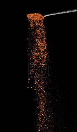 Foto de Red Hot Chilli caída, rojo grano chile explotar nube abstracta volar de cuchara de plata. Hermosa semilla completa fría, diseño de objetos alimenticios. Congelación de enfoque selectivo tiro fondo negro aislado - Imagen libre de derechos
