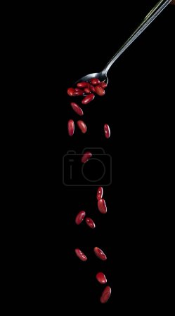 Foto de Caída del frijol rojo, granos rojos explotan nube abstracta volar de cuchara de plata. Hermosa semilla de guisante completa, diseño de objetos alimenticios. Congelación de enfoque selectivo tiro fondo negro aislado - Imagen libre de derechos