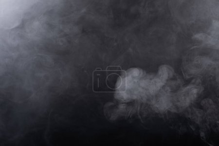 Téléchargez les photos : Bouffées denses de fumée blanche et de brouillard sur fond noir, nuages de fumée abstraits, mouvement flou. Fumeurs soufflant de la machine mouche de glace sèche flottant dans l'air, texture effet - en image libre de droit