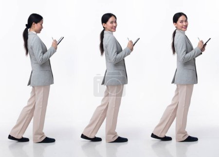 Foto de 20s de longitud completa mujer asiática usar zapatos de pantalón de vestir de traje de chaqueta de negocios formal. Negro pelo largo hembra mantenga tabletas trabajo seguro, caminando hacia adelante gire a la izquierda a la derecha, fondo blanco aislado - Imagen libre de derechos